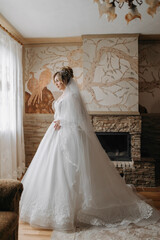 Fototapeta premium A blonde bride in a white dress and a long veil is posing by the window. Beautiful hands. French manicure. Beautiful hair and make-up. Diadem. Daylight