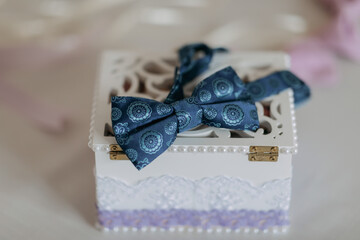 Fototapeta na wymiar The groom's blue butterfly is standing on a wooden box with wedding rings on a white background. Wedding details. Style.