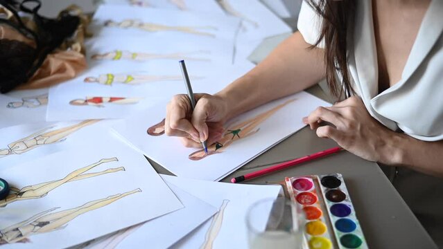 Faceless woman draws sketches of swimwear with a pencil. Close-up of the hands of a fashion designer.