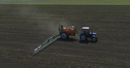 Field works. Tractor spraying on field with sprayer, herbicides and pesticides. Farm machinery spraying insecticide to the field. Modern agroculture at drone view.