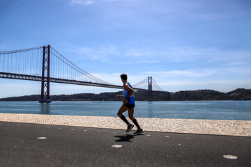 Person running by the river. Ponte 25 de Abril, Lisbon, Portugal