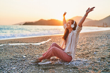 Fototapeta na wymiar Happy woman with open arms and closed eyes enjoys of listening relax traveling music on the seashore at sunset time