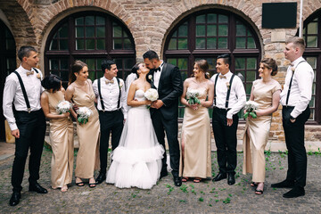 Handsome brunette groom kissing beautiful bride in wedding dress with bridesmaids bouquet and...
