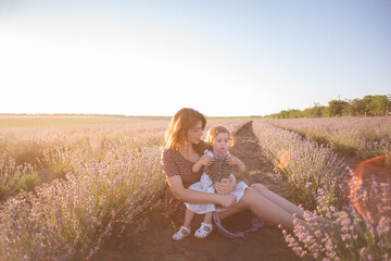 Portrait of brunette mother with little daughter sitting in purple lavender field. Young woman in rural dress lovingly embraces, kisses girl. The concept of allergy, travel, single parent. Copy space