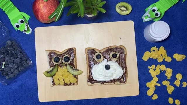 Owl and bear chocolate spread on the bread with fruits moving on the wooden board. Creative kids breakfast concept, intro stop motion. High quality 4k footage