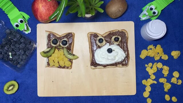 Owl and bear chocolate spread on the bread with fruits moving on the wooden board. Creative kids breakfast concept, intro stop motion. High quality 4k footage