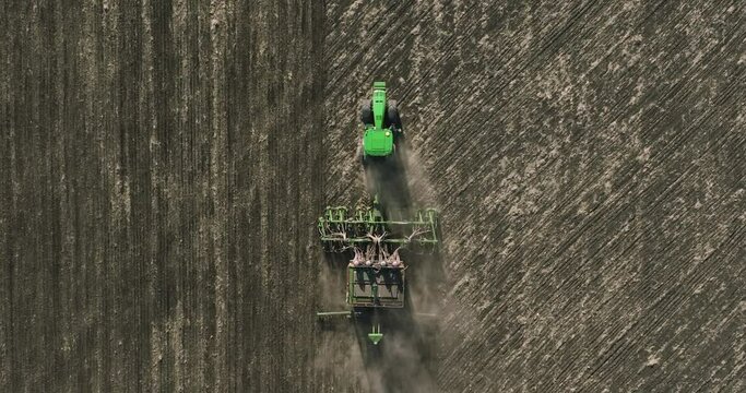 Field works. Tractor sowing seeds with seeder driller in field. Process of sowing cereals and other crops. Sowing work in the field. Tractor with seeder performing seeding. Top down drone view.