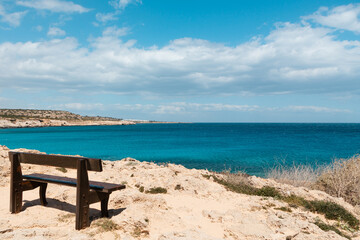 A brown wooden bench on the seashore. View of a beautiful blue lagoon, blue sea water on a sunny day