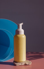 Yellow bottle with a dispenser on a stone on a pink background.