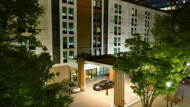 aerial footage flying through lush green trees toward a white hotel with brown wooden trim at night in Buckhead with valets parking cars in Atlanta Georgia USA