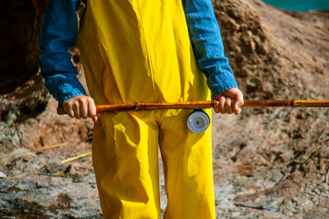 a little fisherman boy with a fishing rod in a yellow fishing jumpsuit