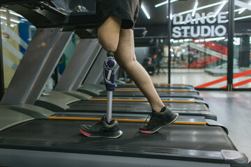 Sports woman with artificial leg running on treadmill at gym. Woman with prosthetic leg using walking on treadmill while working out in gym.