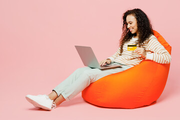 Full body happy smiling young woman she wears casual clothes sit in bag chair using laptop pc...