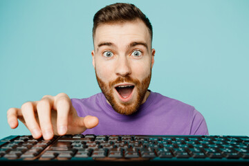 Close up surprised shocked young man he wears purple t-shirt hold use typing on keyboard of pc computer isolated on plain pastel light blue background studio portrait. Tattoo translates life is fight.