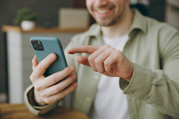 Cropped close up young fun european man wears casual clothes sits alone at table in coffee shop cafe restaurant indoors work hold use mobile cell phone look aside rest relax during free time inside.
