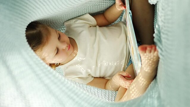 Little girl enjoying of review a book under blue knitted plaid in sunny morning