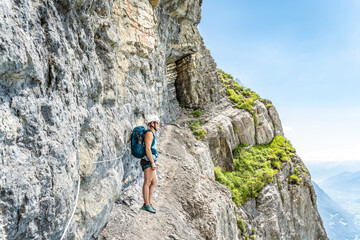 Young woman on rocky hike trail under steep rock wall enjoys view on lake Walensee. Schn&uuml;rliweg, Walensee, St. Gallen, Switzerland, Europe.