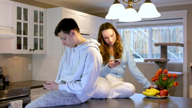 teens sit on table in kitchen girl offended upset pouted boy turned back on phone looks next gadget eat fruit year in background near window adolescence quarrel of discontent offended at each other