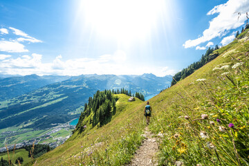 Mountaineer walks on flowery path through a steep meadow with a panoramic view of lake Walensee and the Swiss Alps. Schnürliweg, Walensee, St. Gallen, Switzerland, Europe.