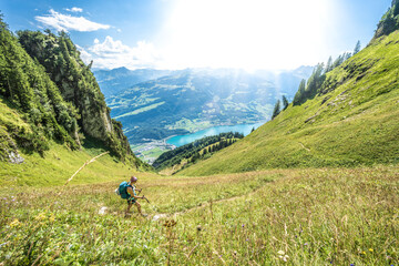 Sporty woman walks on a path through a steep meadow with a panoramic view of lake Walensee and the Swiss Alps. Schnürliweg, Walensee, St. Gallen, Switzerland, Europe.