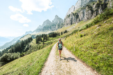 Young woman walks on scenic hiking trail with view on lake Walensee and the Churfürsten mountain...