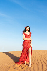 Young beautiful woman in long red dress with red rose petals among the desert. Desert rose conception.