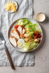 Caesar salad. Healthy salad made with chicken fillet, cherry tomatoes, iceberg lettuce, egg, parmesan cheese and croutons on light grey linen napkin served for one person top view. Light diet dinner