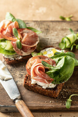 Bruschetta with ham or prosciutto, cream cheese, cucumber, spinach and microgreens. Tasty sandwich or toasted bread on wooden rustic board. Appetizer or breakfast