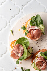 Bruschetta with ham or prosciutto, cream cheese, cucumber, spinach and microgreens. Tasty sandwich or toasted bread on white tile bacground with text space. Appetizer or breakfast, top view, flat lay