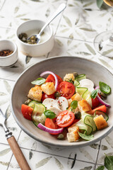 Traditional italian tomato salad panzanella with mozzarella, capers, red onion, croutons, cucumbers and basil. Summer salad on printed tile background