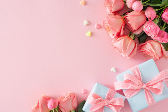 Mother's Day celebration idea. Top view composition of gift boxes with bows bunch of pink roses and small hearts baubles on isolated pastel pink background with copy space
