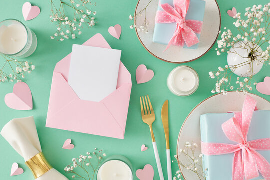 Trendy Mother's Day present concept. Top view photo of plate and cutlery napkin gift boxes candles gypsophila flowers and hearts on turquoise background. Flat lay with open blank envelope for text