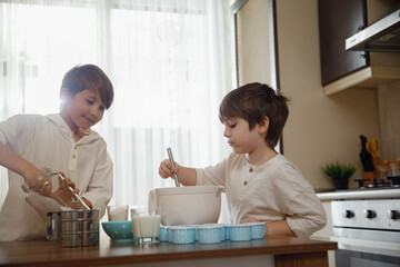 Family activities for kids. Two little boys, brothers make homemade cupcakes,  preparing dough for muffins at the domestic kitchen.