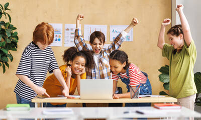 Cheerful  schoolkids   looking at laptop screen and celebrate   successful completion of collective...
