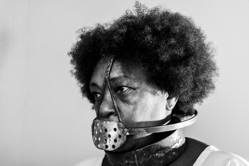 Face portrait of black woman with iron mask of slavery covering her mouth.