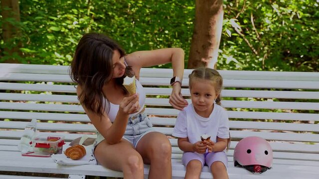 Mother and daughter having snack on bench after skating inline roller in public park together. Family leisure sport activity weekend.  Generative AI