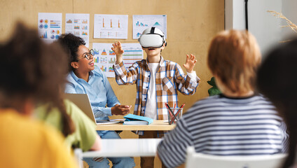   Innovation in education. Student schoolboy in virtual reality glasses together with teacher during lesson in classroom at school.