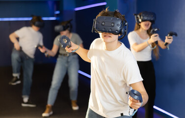 in gaming club, male teen in virtual reality helmet enthusiastically overcomes difficult moment in strategy game simulator. benefits of virtual reality headset