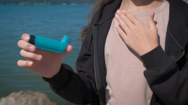 Teen with breathing asthma outdoor. A view of child hand with inhaler during hard breathing attack on the sunny shore. A concept of asthma or health problems during childhood.