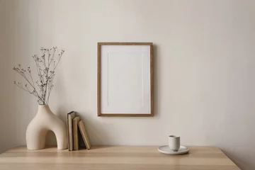  Empty wooden picture frame mockup hanging on beige wall background. Boho shaped vase, dry flowers on table. Cup of coffee, old books. Working space, home office. Art, poster display. Modern interior. © tabitazn