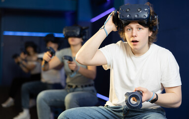 Cheerful emotional young guy in VR headset on head with joysticks in hands looking with excited expression 