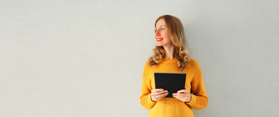 Portrait of happy smiling young caucasian woman with tablet pc or e-book on gray background