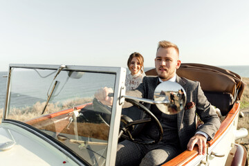 newlyweds driving convertible retro car on country road for their honeymoon, side view. sea...
