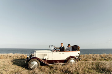 newlyweds driving convertible retro car on country road for their honeymoon, side view. sea...