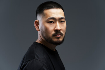 Dramatic portrait of handsome serious asian man with stylish hair, beard looking at camera, isolated on black background