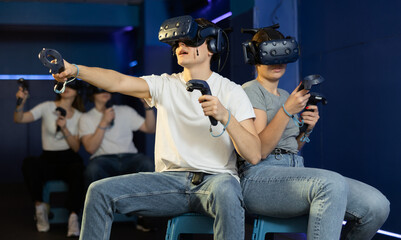 Excited couple, young girl and guy, with handheld controllers in hands engaged in virtual world...