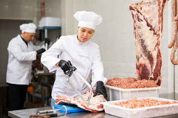 Young female butcher sawing beef ribs with saw