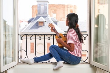 Indian woman playing ukulele on windowsill