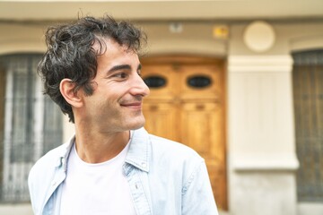 Young handsome caucasian man at outdoor looks aside smiling, cheerful and pleasant.