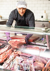 Diligent male butcher offering to sell big piece of beef beef in butcher shop